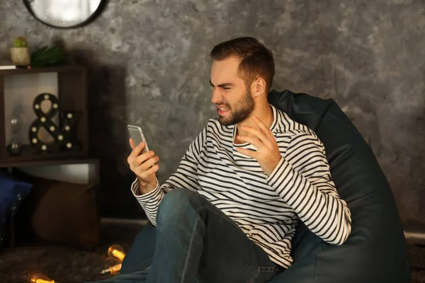 Angry man with mobile phone sitting at home