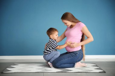 Sevimli küçük çocuk halı üzerinde oturan annesi hamile karnına dokunmak
