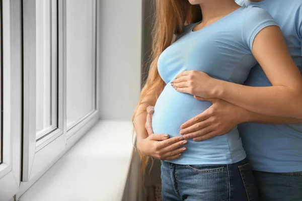 年轻的怀孕夫妇在窗口附近在家 — 图库照片