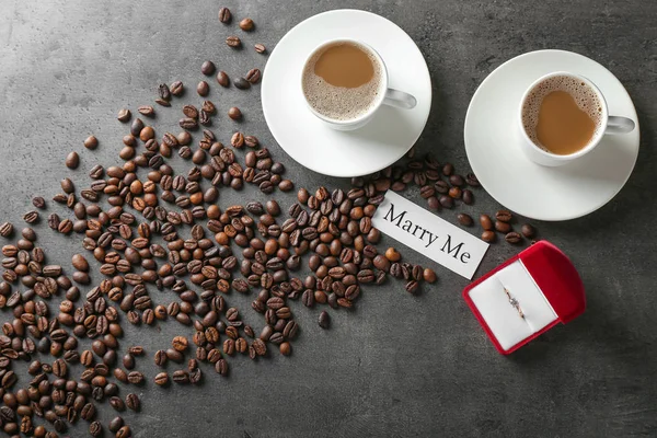 Box with beautiful engagement ring and coffee on grey table