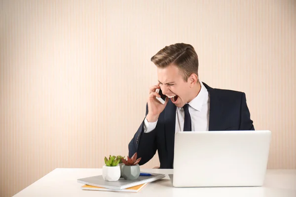 Stressed young businessman talking on mobile phone at table