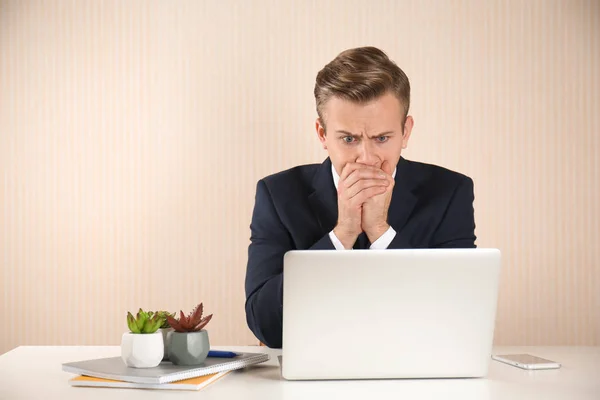 Stressed young businessman at table on light background