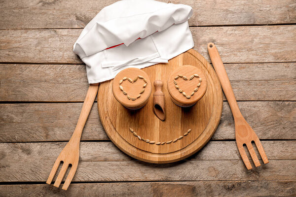 Творческая композиция с шапкой шеф-повара, разделочной доской и кухонной утварью на деревянном фоне
