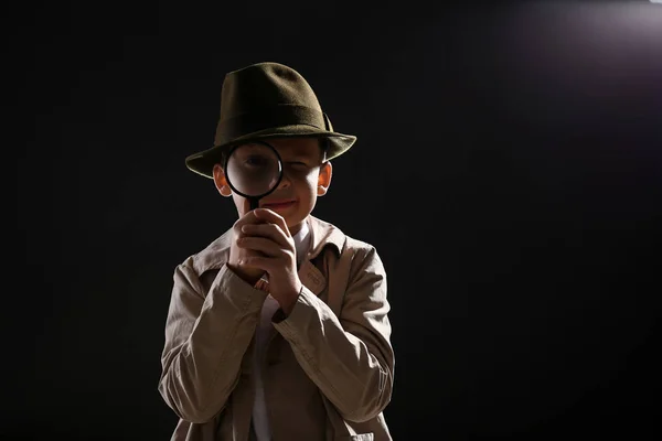Cute little detective with magnifying glass on dark background