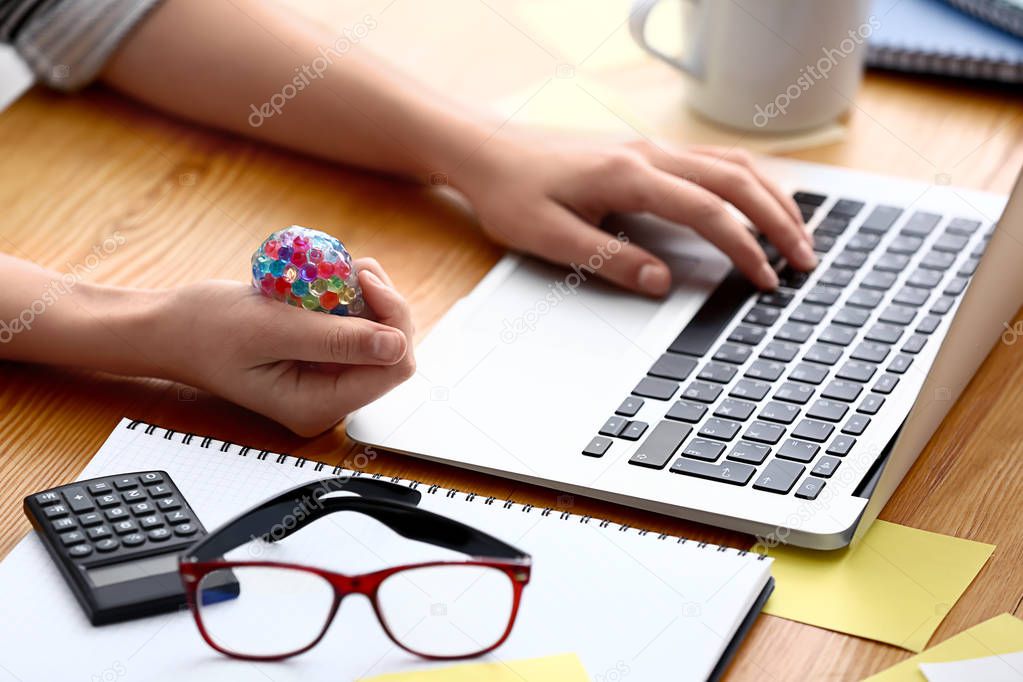 Woman squeezing stress ball while working with laptop