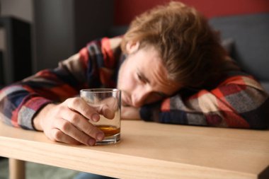 Bardak viski masada olan sarhoş genç adam. Alkolizm kavramı