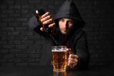 Bira cam siyah duvara yakın masada içine dökülen adam. Alkolizm kavramı