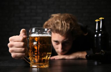 Siyah duvara yakın masada bira ile sarhoş genç adam. Alkolizm kavramı