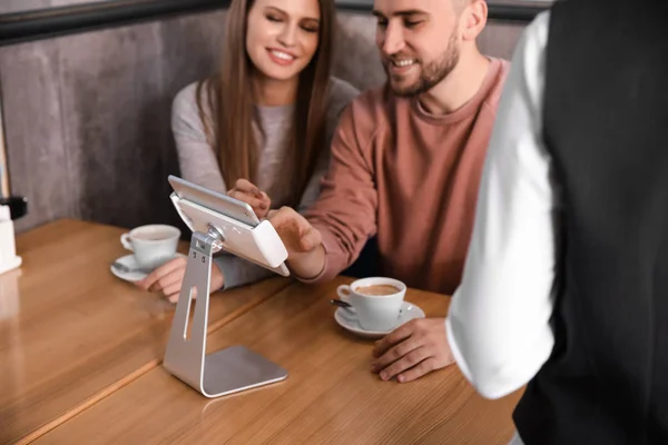 Young couple with tablet PC ordering food in restaurant