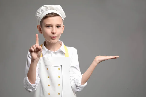 Cute Little Chef Podniesionym Palcem Wskazującym Trzyma Coś Szarym Tle — Zdjęcie stockowe