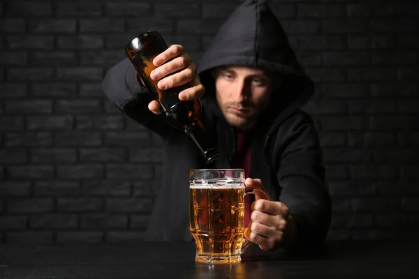 男は黒レンガの壁の近くのテーブルにグラスにビールを注ぐします アルコール依存症の概念 — ストック写真