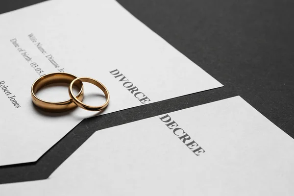 Torn divorce decree with rings on dark background