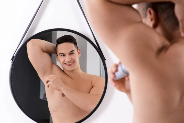 Young man using deodorant in front of mirror