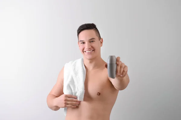 Young man with deodorant on light background