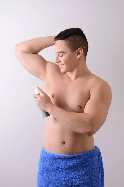 Young man using deodorant on light background