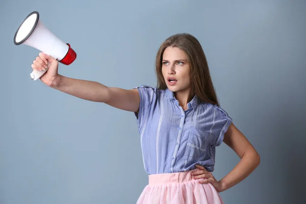 Young woman with megaphone on color background