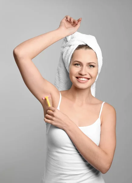 Beautiful young woman shaving armpits on grey background