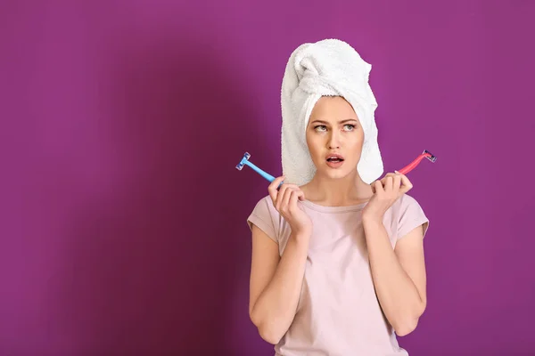 Thoughtful young woman with razors on color background