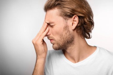 Genç adam ışık arka plan üzerinde baş ağrısı muzdarip