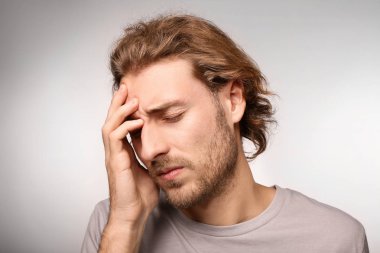 Genç adam ışık arka plan üzerinde baş ağrısı muzdarip