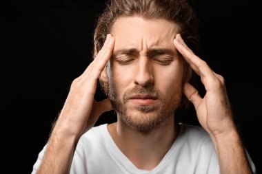 Genç adam koyu arka plan üzerinde baş ağrısı muzdarip