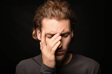 Genç adam koyu arka plan üzerinde baş ağrısı muzdarip