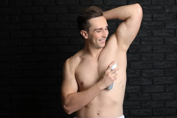 Handsome young man with deodorant on dark background