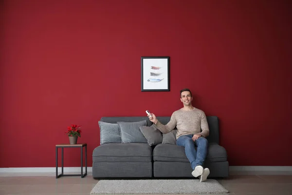 Young man with air conditioner remote control sitting on sofa at home