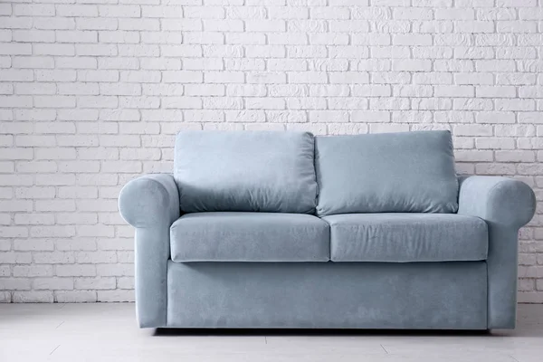 Comfortable sofa near light brick wall in room