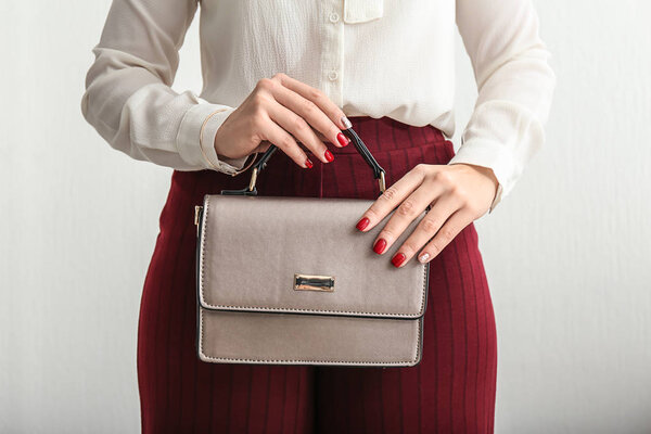 Молодая женщина в формальной одежде держит стильную сумку на светлом фоне
