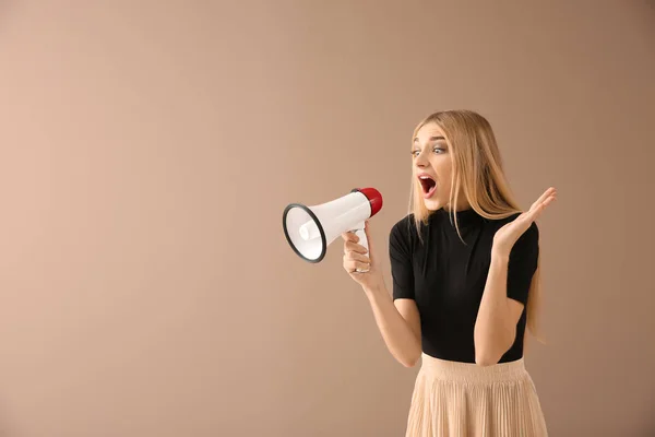 Emotional young woman with megaphone on color background