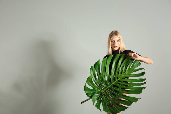 Portrait of beautiful woman with green tropical leaf on light background