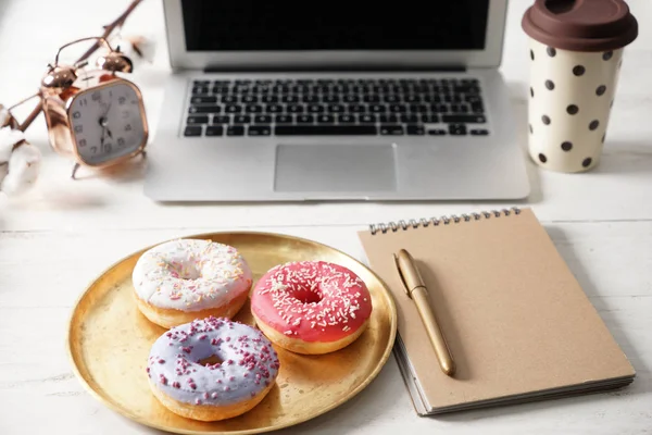 Tray with tasty doughnuts, notebook and laptop on white wooden table