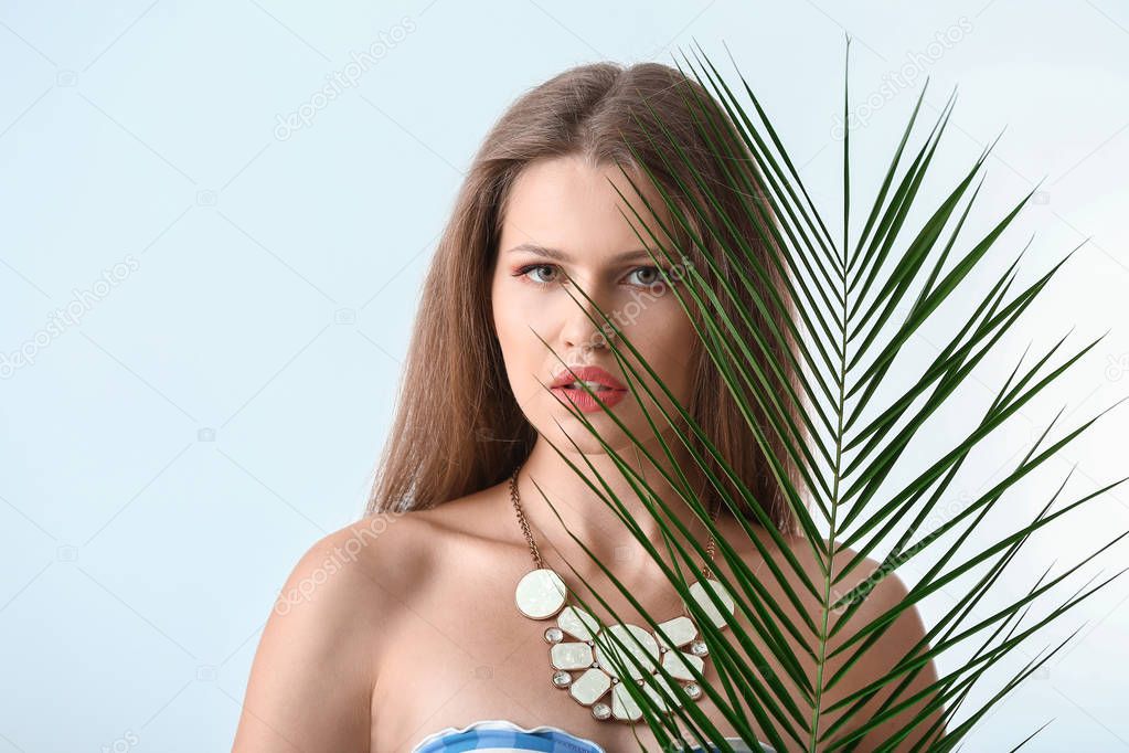 Portrait of beautiful woman with green tropical leaf on light background