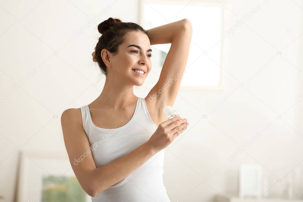 Young woman using deodorant at home