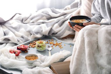 Kadın lezzetli granola ve yatağın üstüne oturan kase yoğurt ile