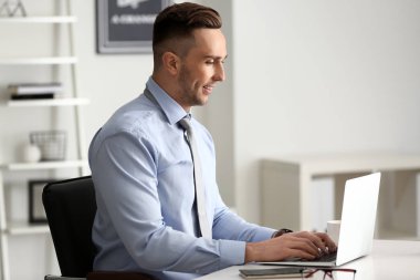 Genç işadamı ofiste dizüstü bilgisayarla çalışıyor.