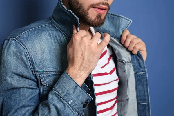 Fashionable young man in jeans jacket on color background, closeup