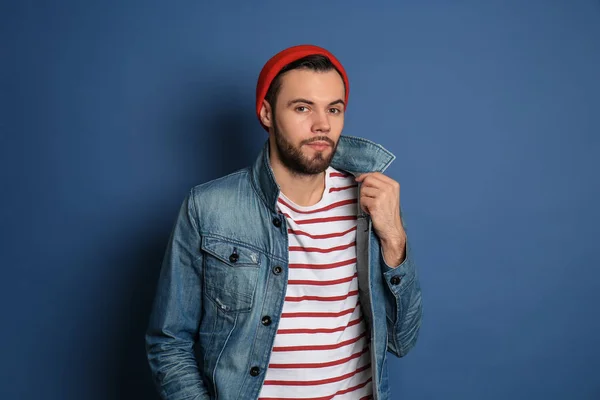 Fashionable young man in jeans jacket on color background