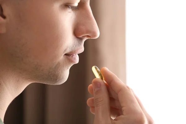 Young man taking pill indoors, closeup