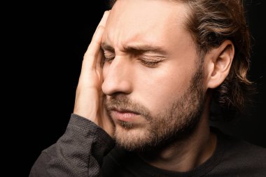 Genç adam koyu arka plan üzerinde baş ağrısı muzdarip