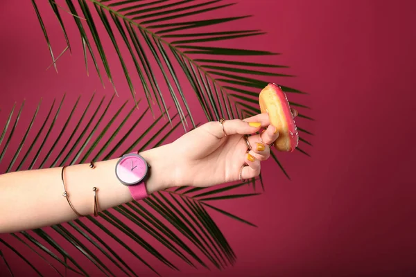 スタイリッシュなアクセサリーと色の背景上のおいしいドーナツと女性の手 — ストック写真