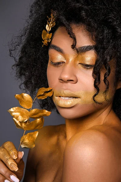 African-American woman with golden paint on her body against dark background