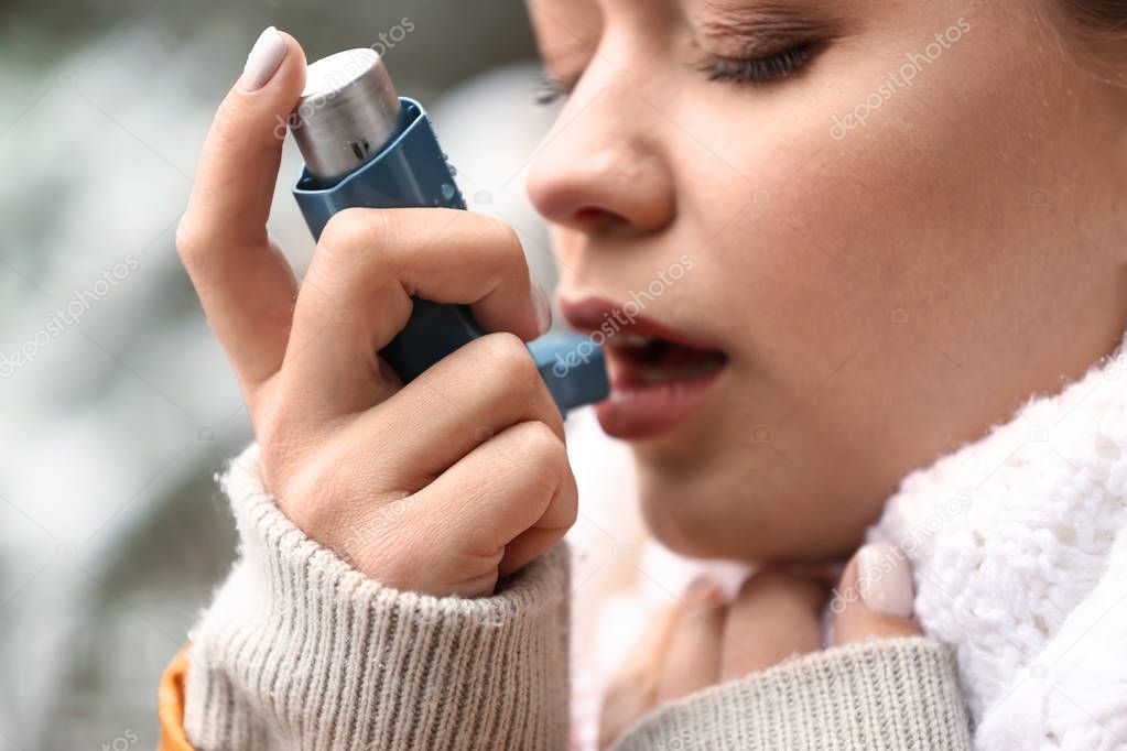 Young woman with inhaler having asthma attack outdoors, closeup