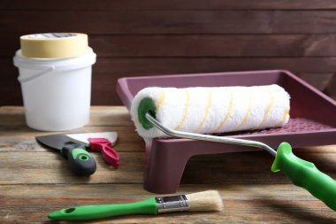 Paint roller in tray and tools on wooden table clipart