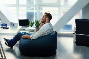 Ofiste beanbag sandalye üzerinde oturan genç işadamı