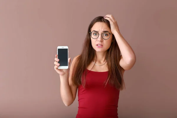 Stressed young woman with non-working mobile phone on color background
