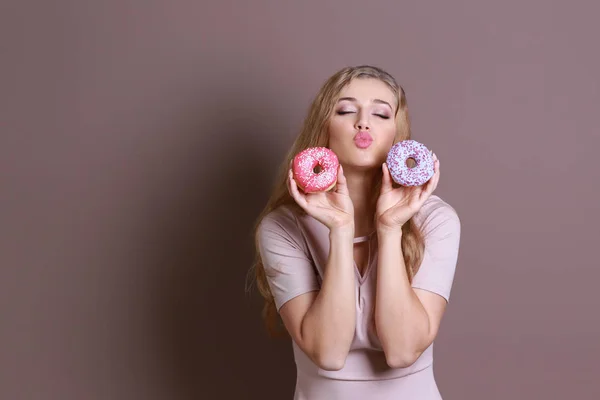 色の背景上のおいしいドーナツを持つ面白い若い女性 — ストック写真