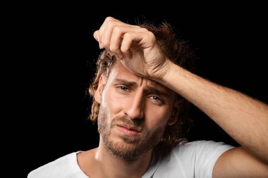 Genç adam koyu arka plan üzerinde baş ağrısı muzdarip