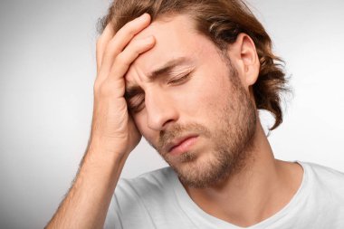 Genç adam ışık arka plan üzerinde baş ağrısı muzdarip